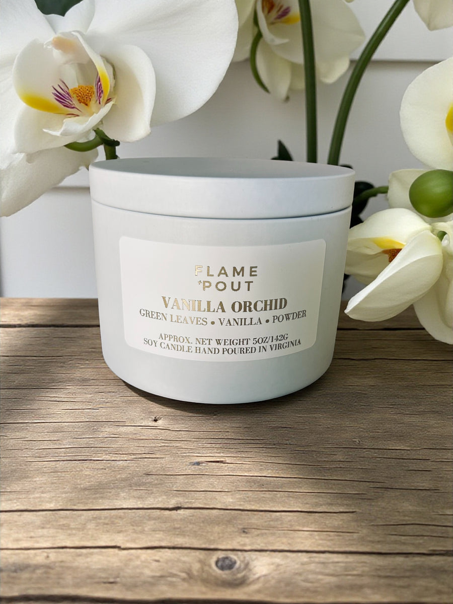 Candle labeled 'Vanilla Orchid' on a wooden surface with white flowers in the background